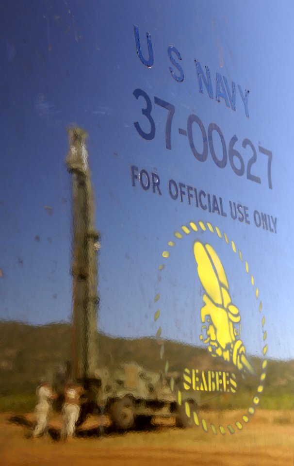 US Navy 051121-F-7234P-032 A truck door with the U.S. Navy Seabees' logo reflects U.S. Navy Petty Officer 2nd Class Joseph McCarthy and Petty Officer 1st Class Ryan Barker preparing the well drilling rig