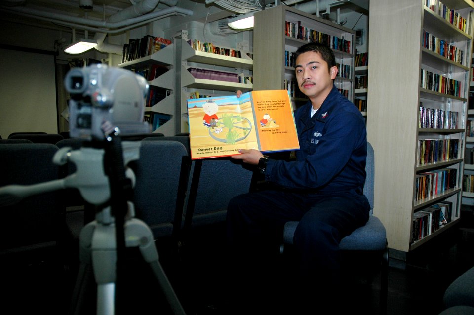 US Navy 051128-N-9866B-606 Ship's Serviceman 2nd Class Billy Amurao reads a children's book into a video camera in the library of the amphibious assault ship USS Peleliu (LHA 5)