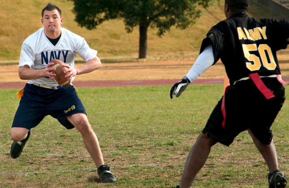 US Navy 051204-N-9851B-005 Cryptologic Technician 3rd Class Cameron Haines, assigned to Seventh Fleet, looks for an open receiver as U.S. Army Sgt. Mark Mullins rushes him at the annual Army vs. Navy flag football game