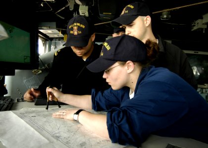 US Navy 060112-N-2385R-133 Lt. j.g. Jason Blackmon and Quartermaster Seaman Jon Smith observe the training being held by Quartermaster 2nd Class Rachael H. Hairston as she updates the navigation charts
