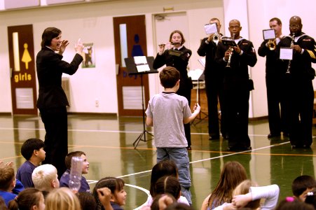 US Navy 060120-N-1194D-006 Chief Musician Roberta Haworth helps a young student direct the Seventh Fleet Band during a rousing concert for the children of Sasebo Elementary School photo