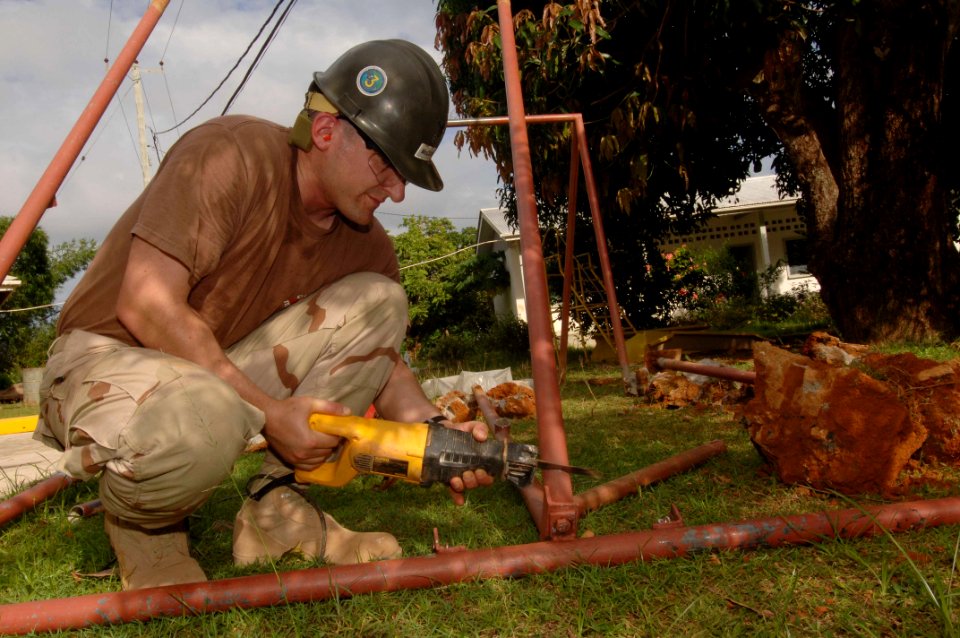 US Navy 051226-N-4374S-018 Hospital Corpsman 1st Class Michael McCune, assigned to Naval Mobile Construction Battalion Three (NMCB-3), cuts an old swing set