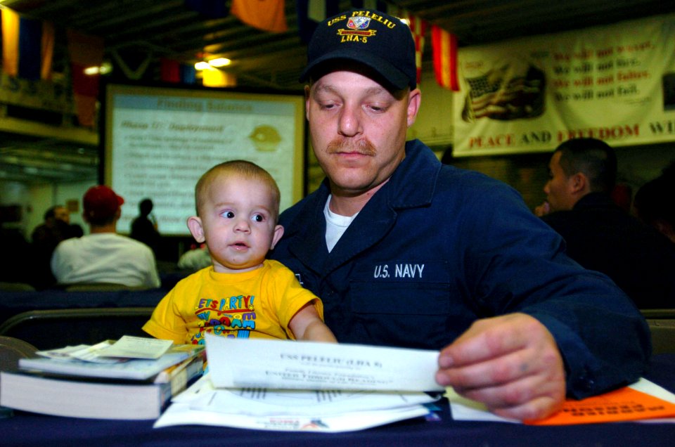 US Navy 060110-N-9866B-012 Deck Seaman Alberto Jimenez looks through handouts with his son during a pre-deployment brief in the hangar bay of the amphibious assault ship USS Peleliu (LHA 5)