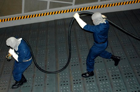 US Navy 060124-N-2736O-012 Two members from the at sea fire party pull an Aqueous Film Forming Foam (AFFF) hose to the scene of a fire aboard the transport dock ship USS San Antonio (LPD 17) during a general quarters drill