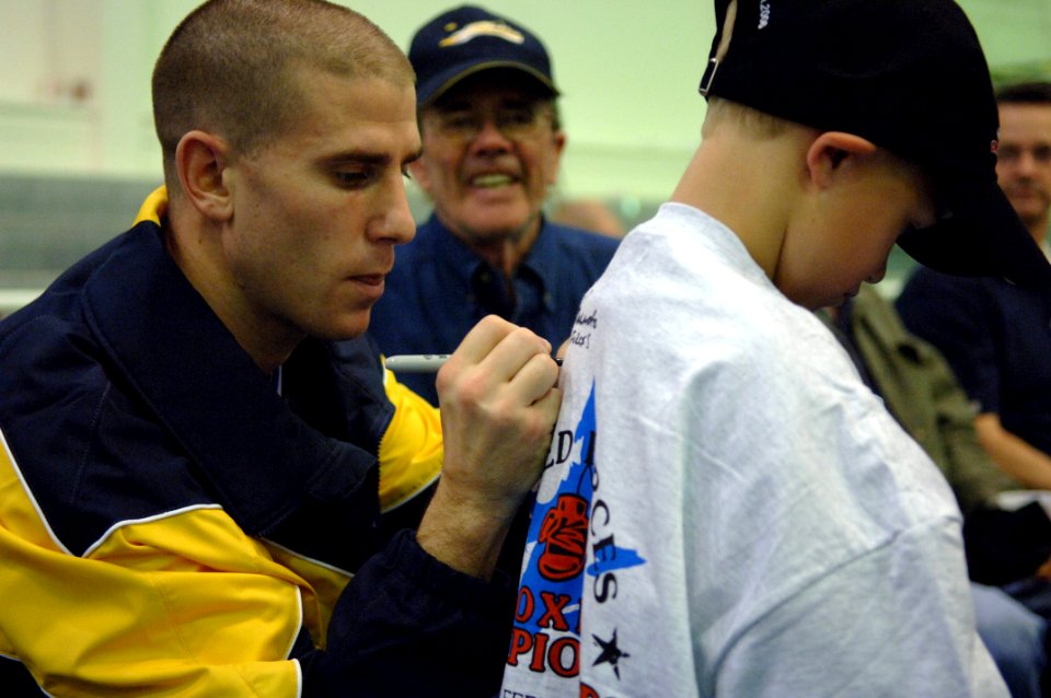 US Navy 060210-N-2653P-349 Aviation Warfare System Operator 2nd Class Adam Fusinato, the 2006 U.S. Armed Forces Champion (152lb) signs the shirt of Navy dependent