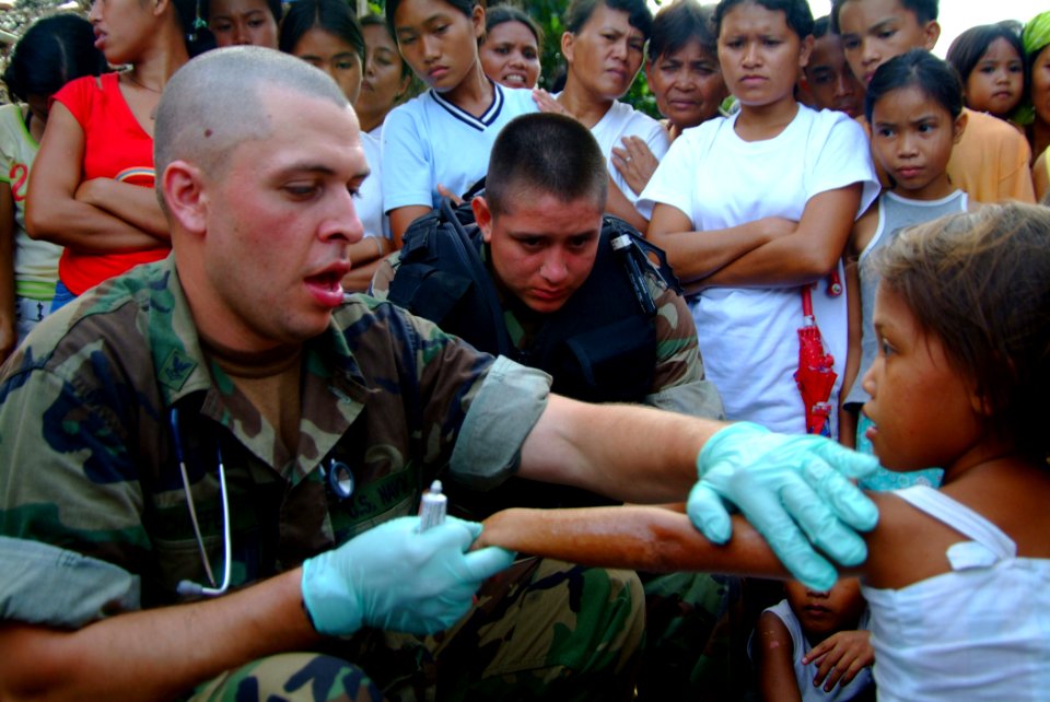 US Navy 060222-N-4772B-181 Hospital Corpsman 2nd Class Eric Schaefer treats a young girl in a small fishing village where Beachmasters have established a landing zone