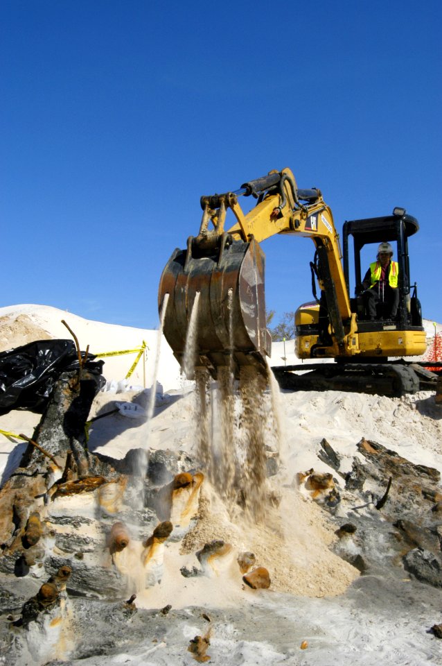 US Navy 060324-5328N-N-769 Using a mini excavator, a heavy equipment operator with the Pittsburgh, Pa.-based, Dick Corp. carefully covers the remains of a wrecked wooden ship aboard Naval Air Station Pensacola