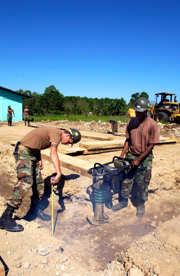 US Navy 060223-F-2326B-078 U.S. Navy Seabee Builder Construction Marc Verno measures the trench depth as Construction Electrician 3rd Class Justin Nice operates the wacky packer
