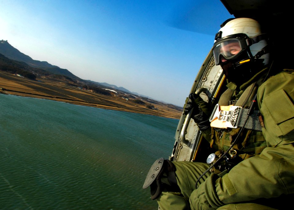 US Navy 060328-N-6074Y-093 Aviation Warfare Specialist 2nd Class Zack Webb, an air crewman assigned to Helicopter Anti-Submarine Squadron Two (HS-2) Golden Falcons, crouches in the door of an SH-60F helicopter