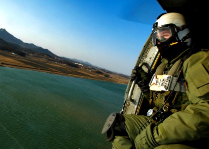 US Navy 060328-N-6074Y-093 Aviation Warfare Specialist 2nd Class Zack Webb, an air crewman assigned to Helicopter Anti-Submarine Squadron Two (HS-2) Golden Falcons, crouches in the door of an SH-60F helicopter