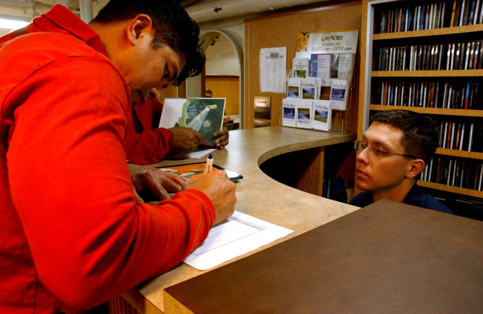 US Navy 060225-N-7711S-109 Master Chief Aviation Ordnanceman Patrick Ponciano checks out a book from the library aboard the Nimitz-class aircraft carrier USS Ronald Reagan (CVN 76) to read to his children for the United Through