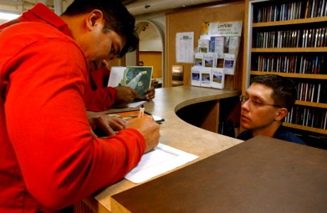US Navy 060225-N-7711S-109 Master Chief Aviation Ordnanceman Patrick Ponciano checks out a book from the library aboard the Nimitz-class aircraft carrier USS Ronald Reagan (CVN 76) to read to his children for the United Through