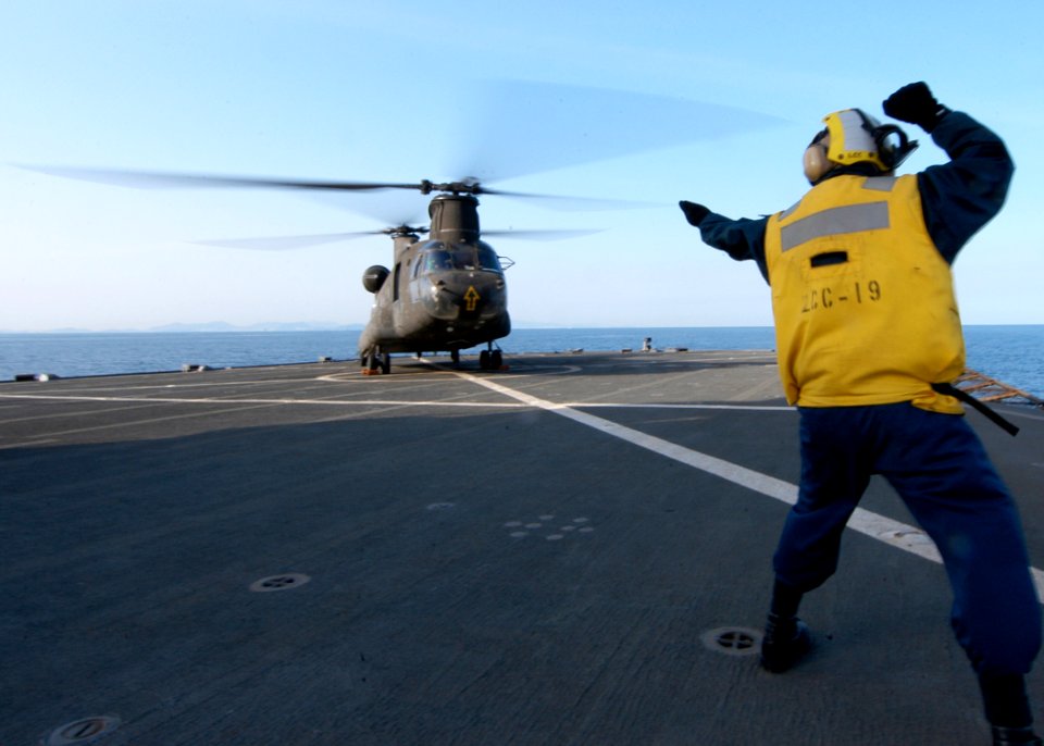 US Navy 060321-N-7526R-035 Boatswain's Mate 2nd Class Edgardo Bauzon signals to an Army CH-47 Chinook helicopter assigned to the 52nd Aviation Regiment from Camp Humphreys Korea, to land on the flight deck of the amphibious co