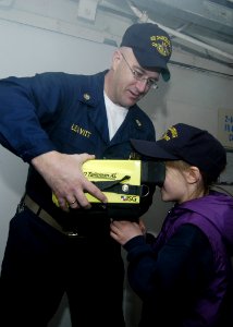 US Navy 060406-N-2385R-141 Chief Damage Controlman Ted Leavitt assists a young visitor aboard the guided-missile cruiser USS Chancellorsville (CG 62)