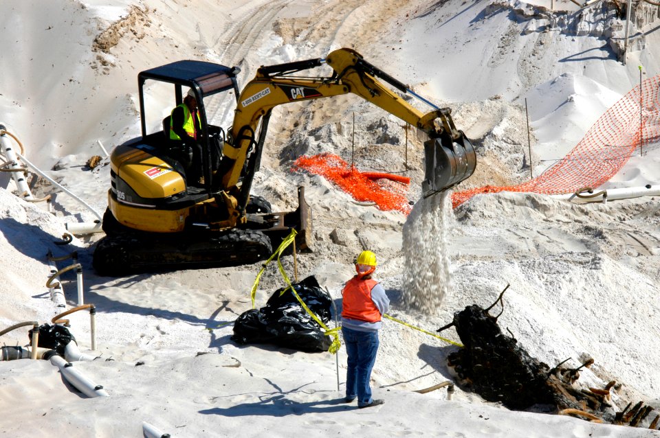 US Navy 060324-5328N-N-324 Using a mini excavator, a heavy equipment operator with the Pittsburgh, Pa.-based, Dick Corp. carefully covers the remains of a wrecked wooden ship aboard Naval Air Station Pensacola
