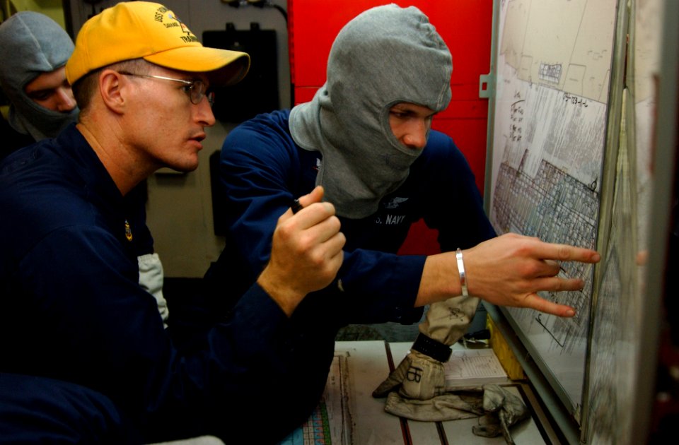 US Navy 060405-N-4776G-173 Damage Control (DC) Repair Locker Leader, Senior Chief Hull Maintenance Technician Frank Furry, lends his knowledge of plotting to Photographer's Mate 3rd Class Aaron Burden