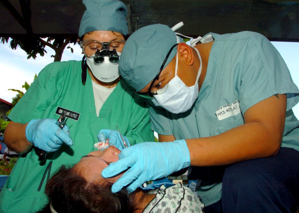 US Navy 060528-N-8391L-081 U.S. Navy Dentist Cmdr. Jan DeLorey-Lytle, left, and Hospital Corpsman 3rd Class Rolando Ambat perform a tooth extraction during a dental assistance mission