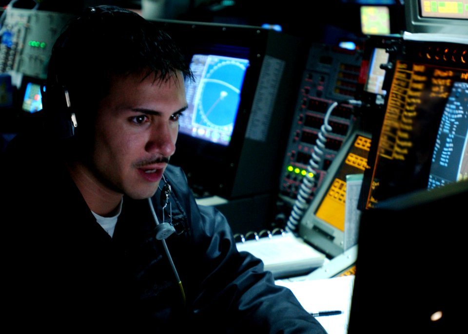 US Navy 060522-N-7526R-001 Operations Specialist 2nd Class Gil Diaz concentrates on a radar screen as he communicates with an aircraft during his air defense weapons coordinator (ADWC) watch, in the Combat Direction Center (CDC