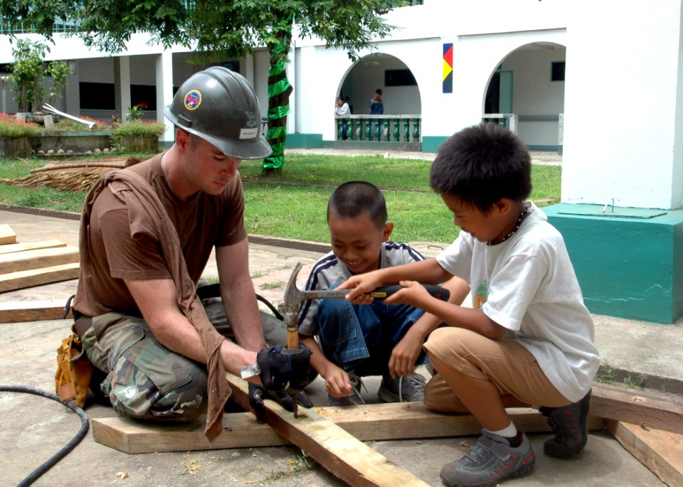US Navy 060606-N-3532C-047 Builder 2nd Class Shane Murray assigned to Naval Mobile Construction Battalion Four Zero (NMCB-40), receives help from some children to build a picnic table for the Sulu Provincial Hospital