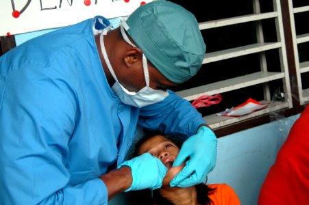 US Navy 060530-N-3153C-010 U.S. Navy Lt. James Harris, a dentist aboard the U.S. Military Sealift Command (MSC) hospital ship, USNS Mercy (T-AH 19) examines the teeth of a young child during a Medical-Dental Civil Action Progra photo