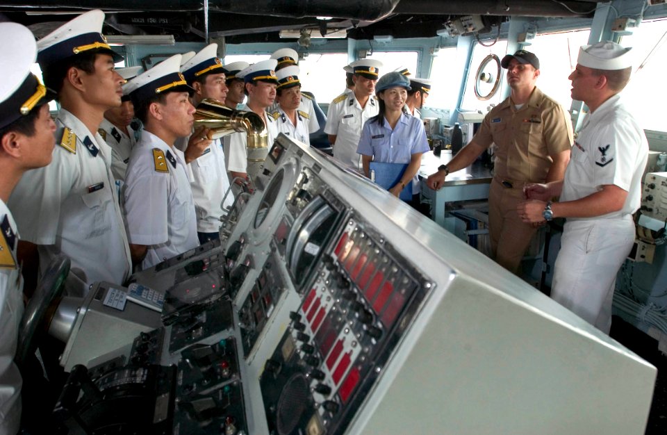 US Navy 060704-N-9851B-003 Quartermaster 3rd Class Robert Arredondo, explains to visitors from the Navy division of the People's Army of Vietnam (PAVN) how rescue and salvage ship USS Salvor (ARS 52) is controlled from the brid