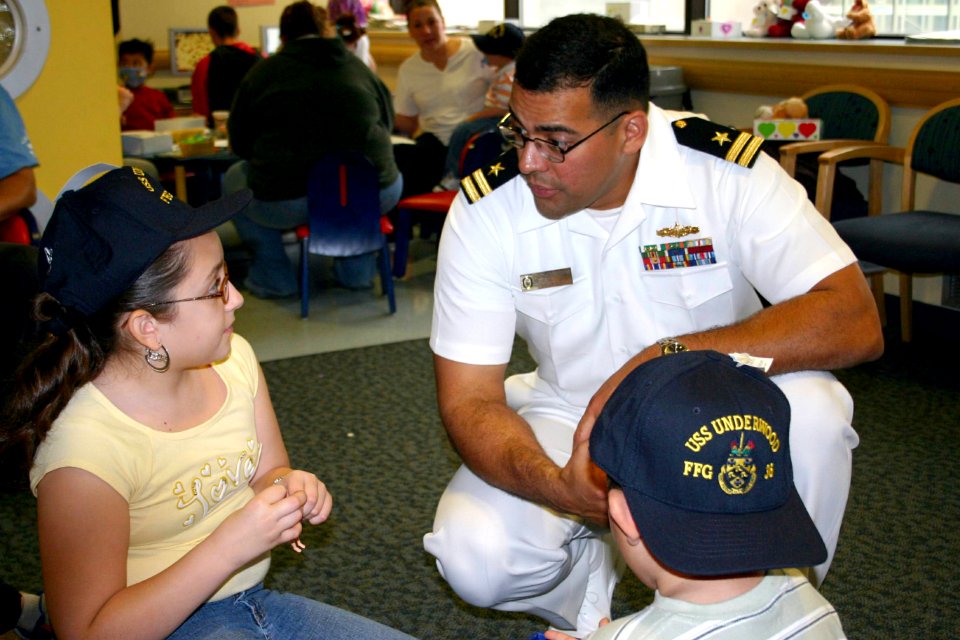US Navy 060609-N-8110K-004 Lt. Orlando Ramos assigned to the guided-missile frigate USS Underwood (FFG 36) speaks with two children at a