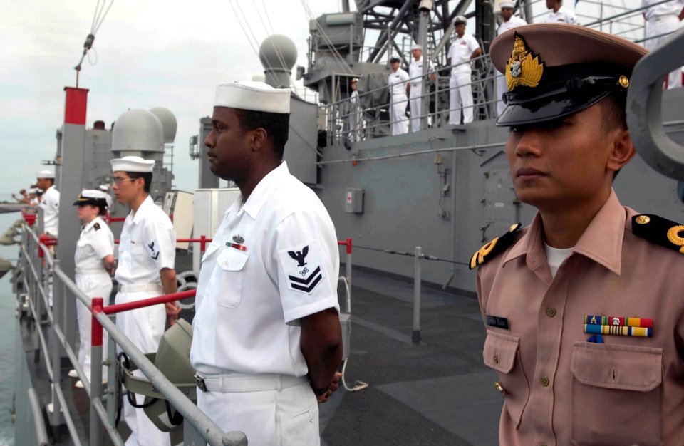 US Navy 060618-N-9851B-004 Royal Thai Navy Liaison Officer, Lt. Ittikorn Buanuam, right, stands with USS Tortuga (LSD 46) Sailors manning the rails as the amphibious dock landing ship enters port