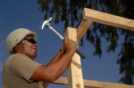 US Navy 060815-N-8623S-026 A Seabee assigned to Naval Mobile Construction Battalion Four Zero (NMCB-40) drives a nail into the framework of a generator shelter outside the command's headquarters