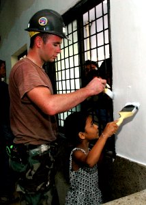 US Navy 060702-N-3714J-101 Navy Builder 2nd Class Shane Murray from Poughkeepsie, N.Y., assigned to Naval Mobile Construction Battalion Four Zero (NMCB-40), receives help from a local girl while painting the pediatric ward at t
