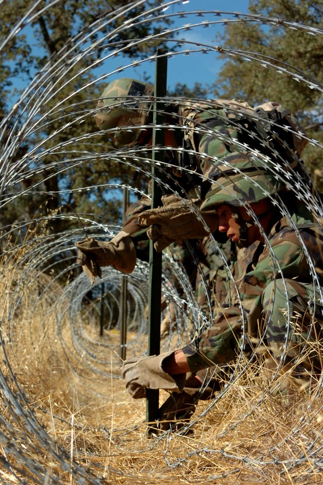 US Navy 060817-N-0775Y-089 Builder 3rd Class Antonio Gonzalez wraps a strand of barbwire to a stake to secure a spool of concertina wire along the outer perimeter of the Logistics Support Area (LSA)