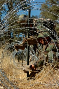 US Navy 060817-N-0775Y-089 Builder 3rd Class Antonio Gonzalez wraps a strand of barbwire to a stake to secure a spool of concertina wire along the outer perimeter of the Logistics Support Area (LSA)
