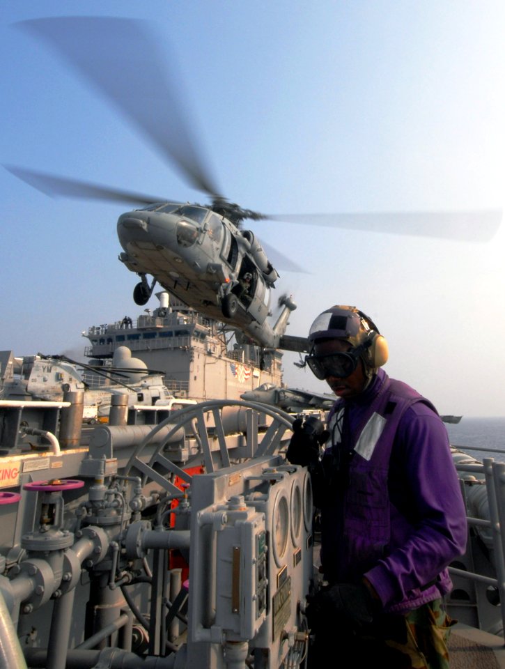 US Navy 060818-N-4856C-018 Airman Travis D. Keys checks fuel gauges just off the flight deck as a MH-60S Seahawk helicopter prepares to land aboard the amphibious assault ship USS Iwo Jima (LHD 7)