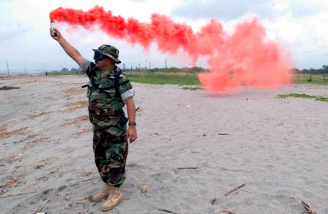 US Navy 060818-N-9851B-001 Chief Boatswain's Mate Victor R. Gonzales of Beach Master Unit One detachment Western Pacific holds a smoke marker to direct a landing craft air cushion (LCAC)