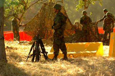 US Navy 060817-N-0775Y-007 Storekeeper Seaman Apprentice Travis Clanton stands a weapons watch while the rest of his crew places camouflage netting over a defensive position at the entrance of the Logistics Support Area