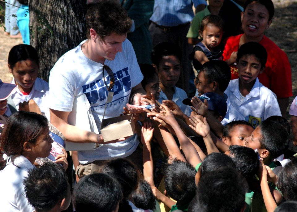 US Navy 060824-N-9076B-134 Project Hope Volunteer Craig Jacques hands out pencils to children during a medical outreach at the Batakte Health Center as part of the Military Sealift Command hospital ship USNS Mercy (T-AH 19) vis