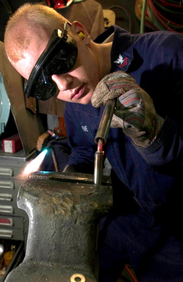 US Navy 060902-N-9851B-007 Hull Technician 2nd Class Benjamin Howe bends the heated end of a metal rod to be used in making a replacement spoke in the steering wheel of a Rigid Hull Inflatable Boat (RHIB)