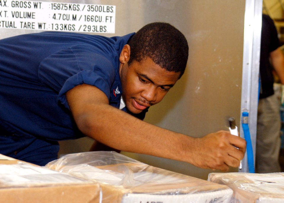 US Navy 060828-N-2716P-009 Postal Clerk 3rd Class Samuel Anderson calls out the destination of an incoming package and marks the parcel accordingly during mail distribution at Fleet Mail Center, Yokohama