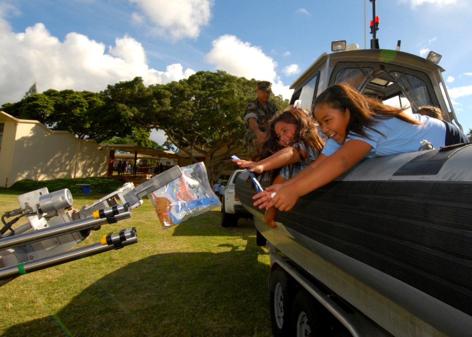 US Navy 061109-N-4965F-003 Engineman 1st Class Rafael Rangel, assigned to Explosive Ordnance Disposal Mobile Unit Three (EODMU-3), watches as two Pearl Kai elementary school students reach from a Mk-5 Rigid Hull Inflatable Boa