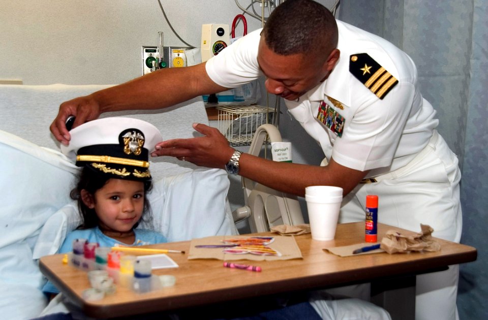 US Navy 061108-N-3750S-160 Cmdr. Brad Lee, commanding officer of USS San Antonio (LPD 17) places his cap on six year-old girl at Methodist Children's Hospital, making her an honorary ship's commander for a day