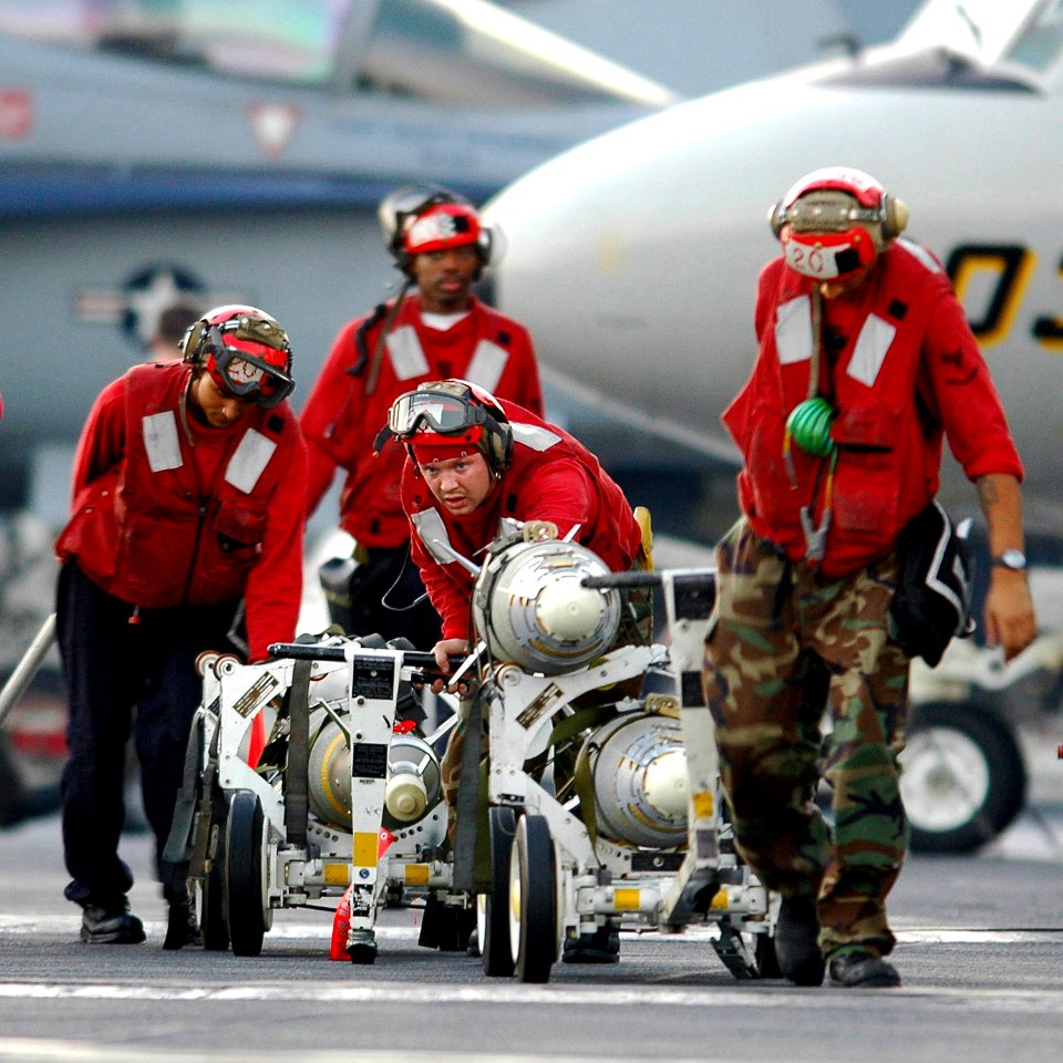 US Navy 061122-N-0490C-002 Aviation Ordnancemen assigned to the Jolly Rogers of Strike Fighter Squadron One Zero Three (VFA-103) transport a Laser Guided Bomb Unit-12 (GBU-12) and two GPS Guided Bombs Unit-38 (GBU