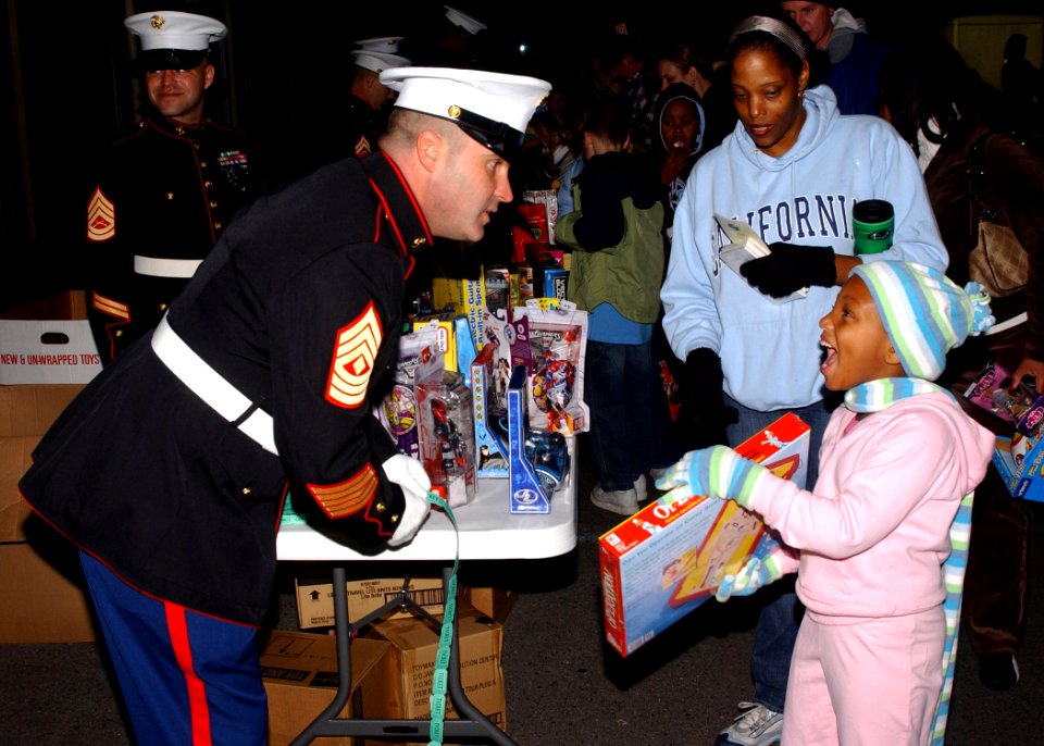 US Navy 061202-N-7427G-001 1st Sgt. John Catalinie gives out toys to a child as part of the Marine Corps Toys for Tots Program at Naval Air Station Joint Reserve Base