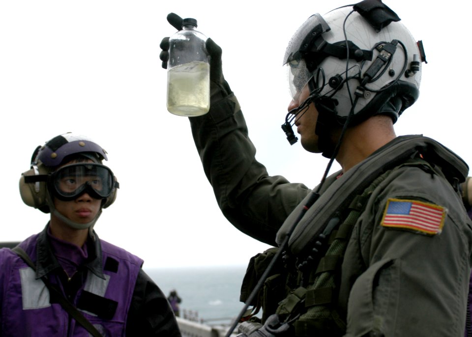 US Navy 061203-N-2636M-157 Aviations Warfare Systems Operator 2nd Class Omar Perez Rodriguez from Helicopter Sea Combat Squadron Two Six (HSC-26) inspects a fuel sample from Airman Minh T. Le while refueling an MH-60 during fli