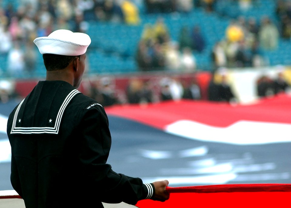 US Navy 061202-N-4565G-003 A Sailor assigned to USS John F. Kennedy (CV 67) holds the National Ensign during the playing of the Nation Anthem during the NCAA Atlantic Coast Conference Championship game at Alltel Stadium
