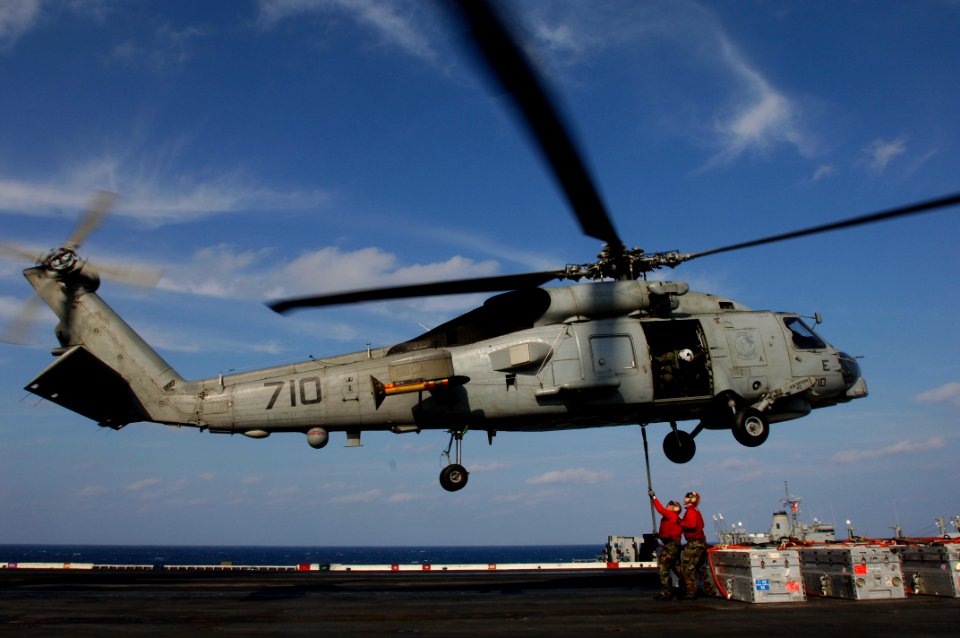US Navy 061206-N-8591H-086 An air crewman watches as two aviation Ordnancemen connect a cargo pendant to a SH-60B helicopter