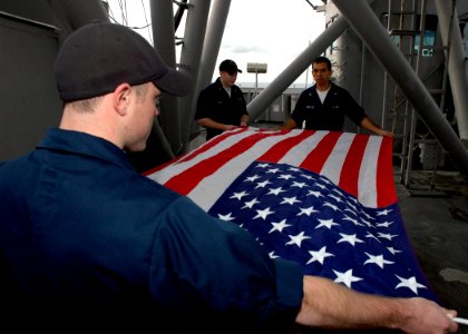 US Navy 061210-N-8547M-009 Quartermaster Seaman Jeff Schulze, Quartermaster 3rd Class Wilfred Gonzalez and Quartermaster 2nd Class Jason A. Lentz fold the National Ensign aboard the amphibious assault ship USS Saipan (LHA 2)