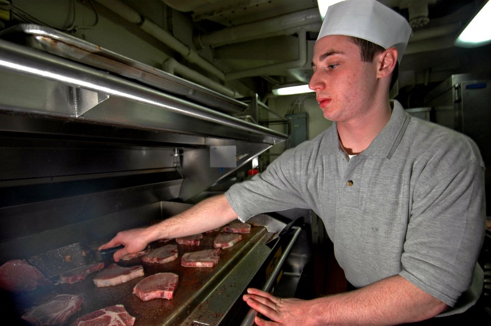 US Navy 070104-N-7883G-006 Culinary Specialist Seaman Rob Exler from Columbia, Md., grills pork chops in the aft galley aboard USS Kitty Hawk (CV 63)