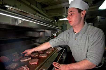 US Navy 070104-N-7883G-006 Culinary Specialist Seaman Rob Exler from Columbia, Md., grills pork chops in the aft galley aboard USS Kitty Hawk (CV 63) photo