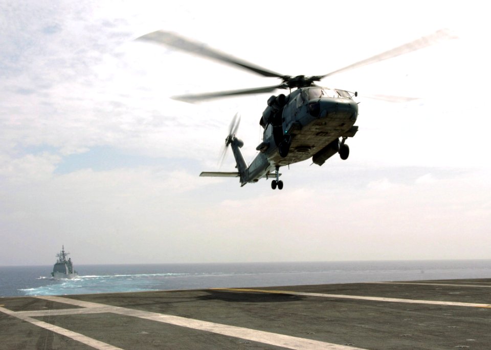 US Navy 070108-N-0490C-001 The Ticonderoga-class guided-missile cruiser USS Anzio (CG 68) steams behind the Nimitz-class aircraft carrier USS Dwight D. Eisenhower (CVN 69) as an SH-60F Seahawk prepares to land on Eisenhower's f