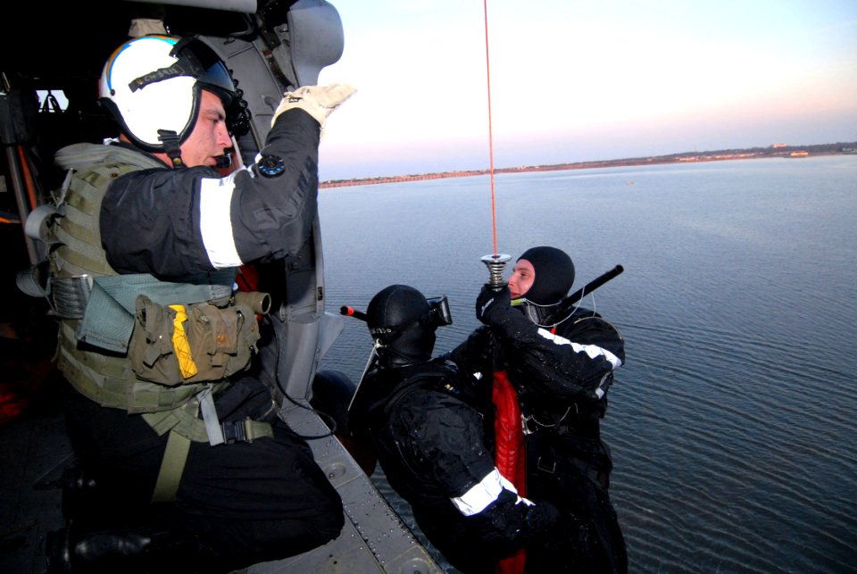 US Navy 070124-N-8704K-082 Aviation Warfare Systems Operator 2nd Class Bryan Wedding, assigned to Helicopter Sea Combat Squadron Two Six (HSC-26), hoists two Sailors into an MH-60S helicopter while simulating search and rescue