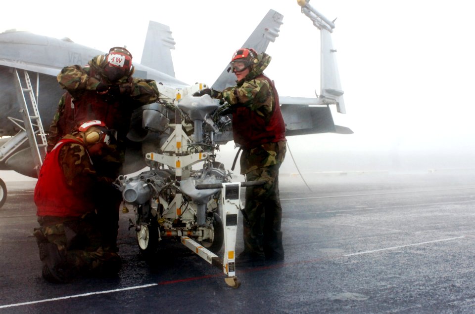 US Navy 070130-N-0555B-189 Braving wind and rain, aviation ordnancemen assigned to Strike Fighter Squadron Two Five (VFA-25) huddle around a bomb rack trying to finish their checks before the rain becomes an impediment to safet